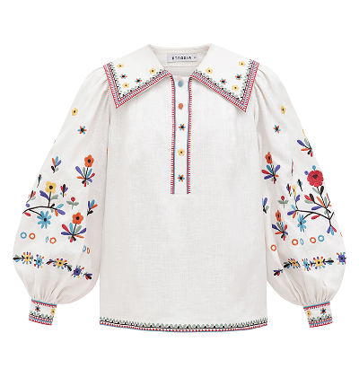 A white linen blouse featuring a large pointed collar, voluminous puff sleeves, and vibrant multi-colored floral and geometric embroidery accented by colorful buttons